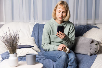 Portrait of young woman using mobile phone while sitting on bed at home