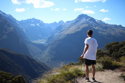 Rear view of man standing on mountain against sky