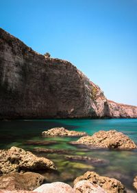 Scenic view of rocks in sea against clear blue sky