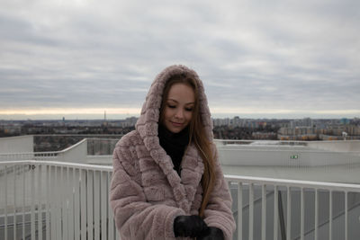 Young woman standing on railing against sky during winter