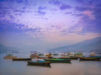 Fishing boats moored in sea against sky at sunset