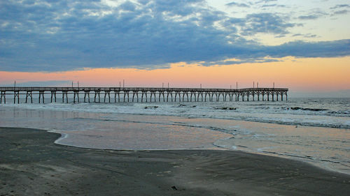 Pier on beach against sky during sunset