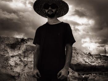 Low angle view of man wearing hat standing against cloudy sky during sunset