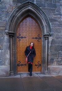 Portrait of woman standing against door of building