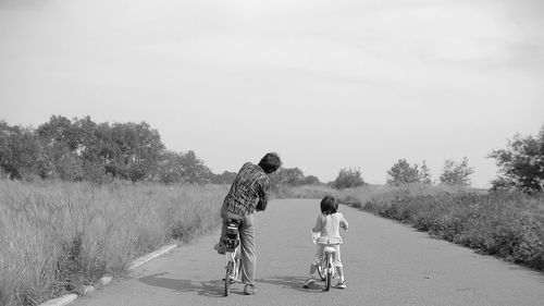 Father and daughter riding bicycle on road amidst field