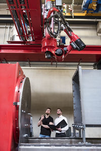 Two men with folder looking at machine on factory shop floor