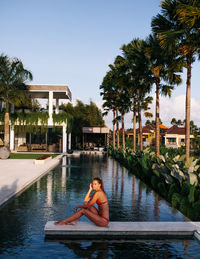 Side view portrait of woman in bikini sitting on footpath over pool at villa