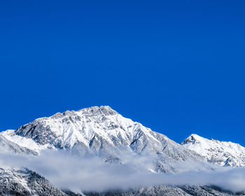 Low angle view of snowcapped mountains against clear blue sky