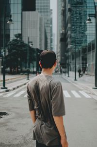 Rear view of man standing on road against buildings in city