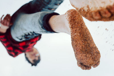 From below upside down view of young hipster female in casual checkered shirt and jeans with wet sand on feet reflected on window standing on beach