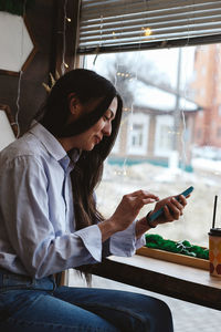 Brunette girl by the window in a cafe with smartphone, social media