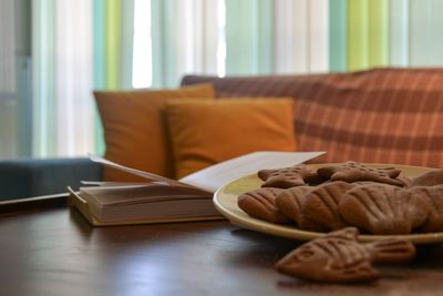 Close-up of open book by cookies in plate on table at home