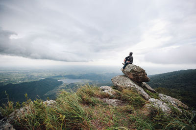 Hiker sitting on rocks against cloudy sky during foggy weather