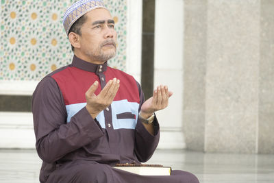 Mature man praying while sitting at mosque