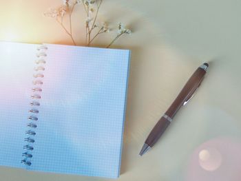 High angle view of pen and blank diary with flower on colored background