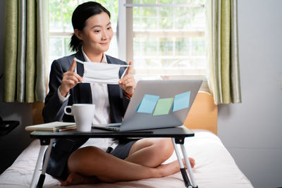 Mid adult woman using mobile phone while sitting on table