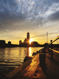 Silhouette city by river against sky during sunset