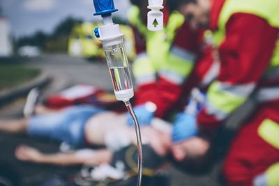 Close-up of iv drip against paramedic giving cpr to unconscious man lying on street