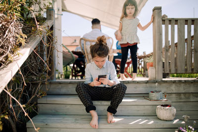 Girl looking at sister using mobile phone while sitting on steps in patio