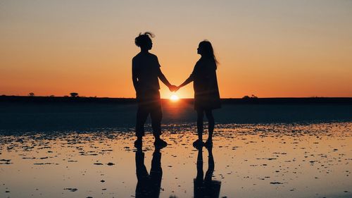 Silhouette woman standing on beach against sky during sunset