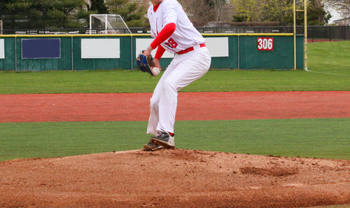 A high school pitcher is in his motion pitching the ball off of the pitching mound during a game.