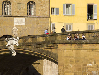 People at ponte santa trinita bridge against buildings