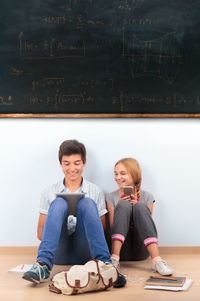 Full length of happy friends sitting in classroom