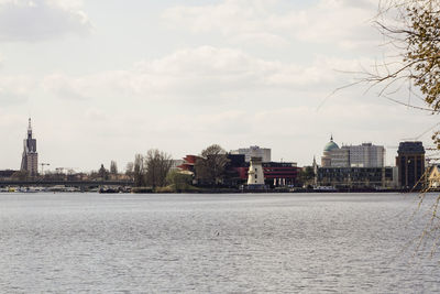 View of buildings by river against cloudy sky