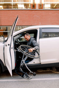Side view of mature man holding wheelchair while sitting in car on city street