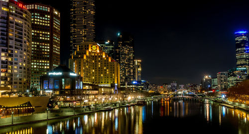 Illuminated buildings by river against sky at night