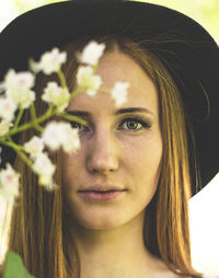 Portrait of young woman with long hair wearing hat by flowers