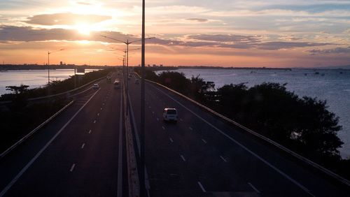 Road by sea against sky during sunset