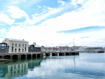 View of buildings by river against cloudy sky