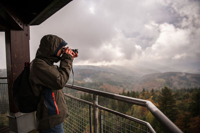 Rear view of man leaning on railing against mountain