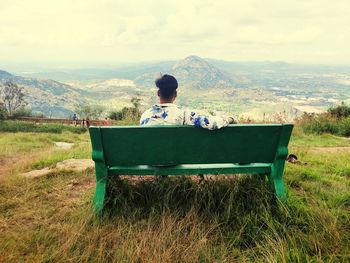 Rear view of man sitting on bench against landscape