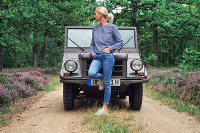 Full length of woman standing by jeep in forest
