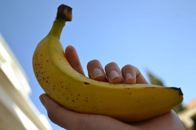 Close-up of hand holding fruit against blue sky