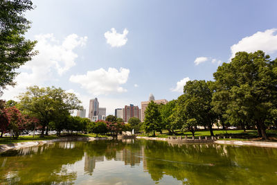 Trees by lake in park against sky in city