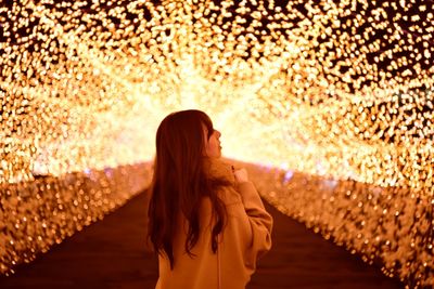 Side view of woman standing at illuminated tunnel
