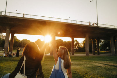 Rear view of teenage girls with hands raised walking against bridge at park