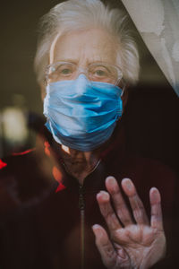 Close-up portrait of senior woman wearing mask looking through window