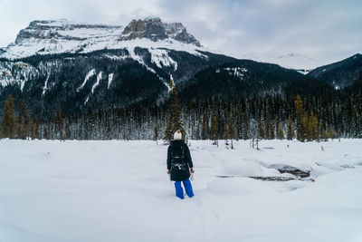 Female hiking in snow-covered landscape with dramatic snow-capped mountains in distance.