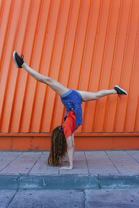 Young woman doing handstand against orange wall