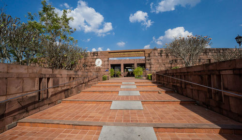 Footpath amidst buildings against cloudy sky