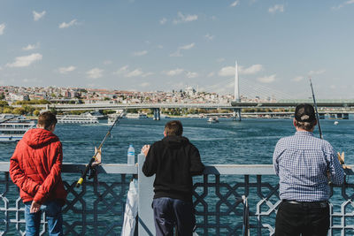 Rear view of men standing on bridge in city against sky