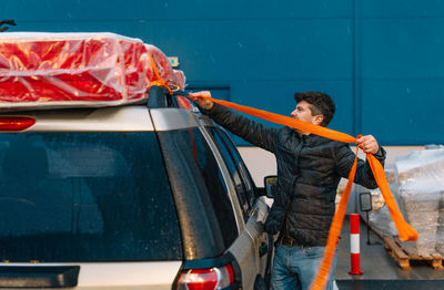 Man securing mattress on car top in a rainy evening