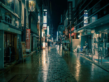 Wet street amidst illuminated city at night