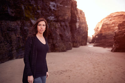 Beautiful woman looking away while standing against rock formation
