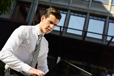 Low angle view of businessman using laptop while sitting in city