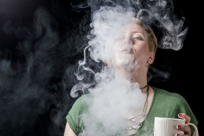 Close-up of woman smoking against black background